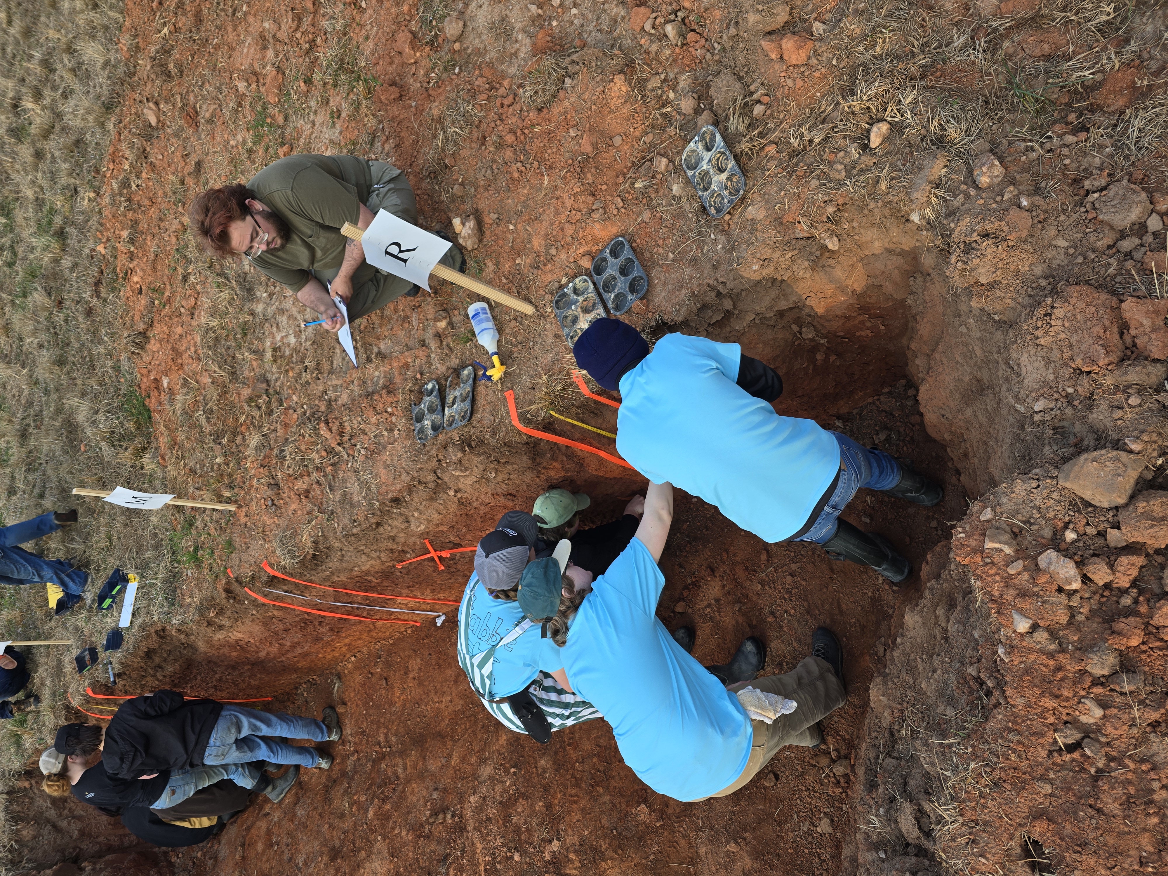 Members of the MSU Soil Judging Team kneel in a pit to inspect the soil.